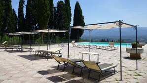 Zona de piscina con tumbonas y sombrillas, rodeada de altos árboles y una vista despejada de las montañas.