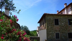Un edificio de piedra con tejado de baldosas, un patio de grava y flores rosadas en primer plano.
