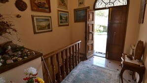 A hallway with a wooden staircase, a blue patterned rug, and various framed artworks on the walls.