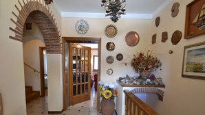 A hallway with a wooden staircase, a tiled floor, and a wooden railing.