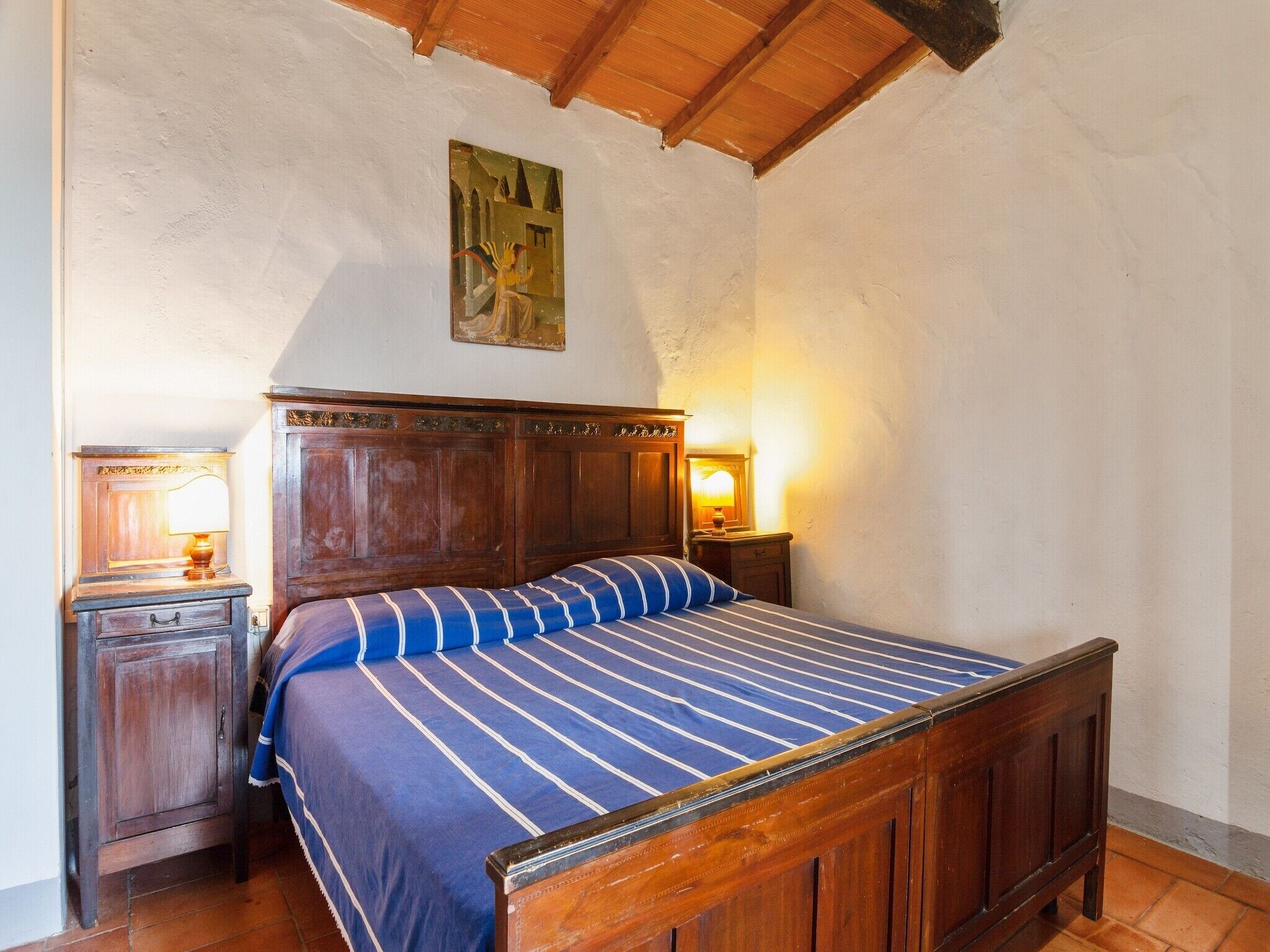 A bedroom with a wooden bed, a nightstand with a lamp, and a painting on the wall.