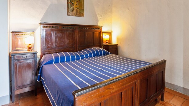 Un dormitorio con una cama de madera, una mesita de noche con una lámpara y un cuadro en la pared.
