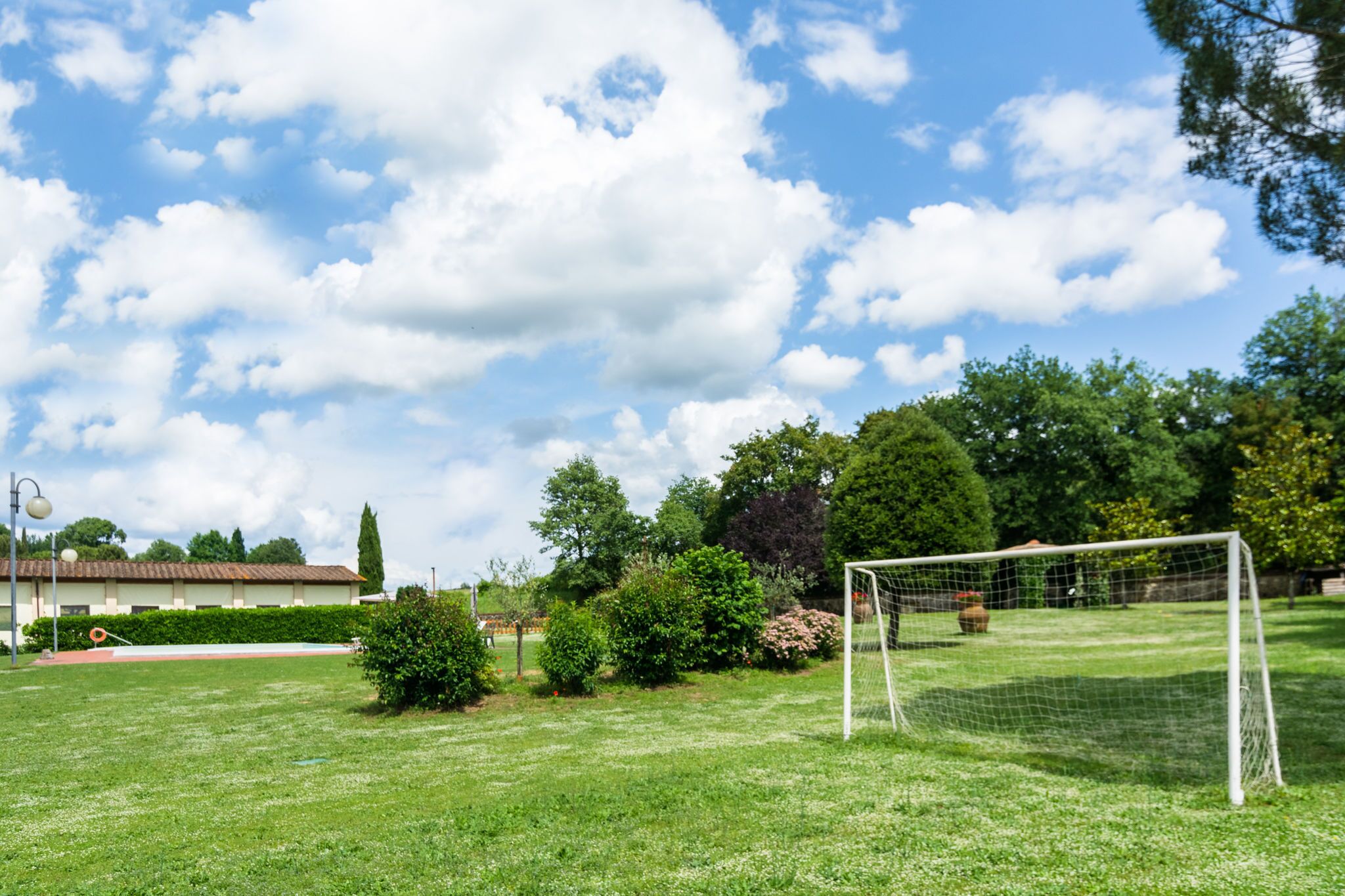 Een grasveld met een voetbaldoel, bomen en een gebouw op de achtergrond.