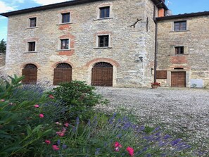 Un bâtiment en pierre doté de nombreuses fenêtres et portes, entouré de gravier et de plantes en fleurs.