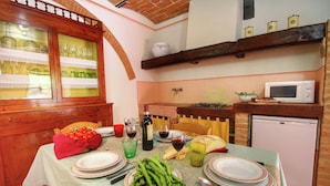 A dining area with a table set for two, featuring plates, cutlery, a bottle of wine, and a bowl of green beans. - Belvilla by OYO Tiglio (Cortona)