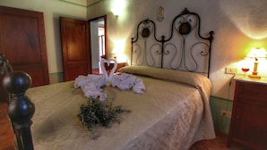 A neatly made bed with a decorative headboard, a wooden door, and a nightstand with a lamp. - Belvilla by OYO Tiglio (Cortona)