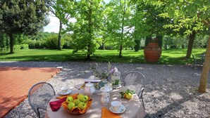 An outdoor dining area with a table set for two, surrounded by trees and a gravel path. - Belvilla by OYO Leccio (Cortona)