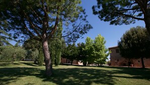 A courtyard with a large tree, a brick building, and a grassy lawn. - Belvilla by OYO Leccio (Cortona)