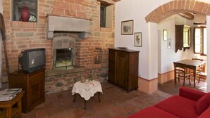 A cozy living room with a brick fireplace, a television, a dining table, and a red sofa. - Belvilla by OYO Leccio (Cortona)