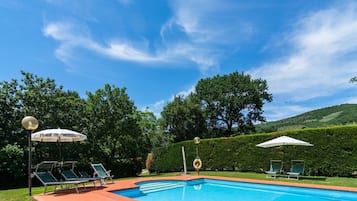 Ein Pool mit Liegestühlen und Sonnenschirmen, umgeben von Grün und Hügeln.