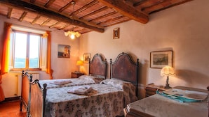 A room with two wooden beds, a wooden dresser, a window with curtains, and a lamp on a nightstand. - Belvilla by OYO Lunghe (Siena)