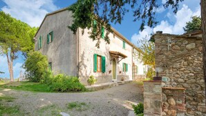 Un edificio rustico in pietra con vialetto sterrato e un piccolo giardino con piante in vaso.
