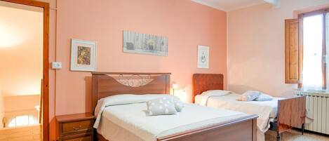 A bedroom with two beds, a wooden headboard, a nightstand, a dresser, and a radiator.
