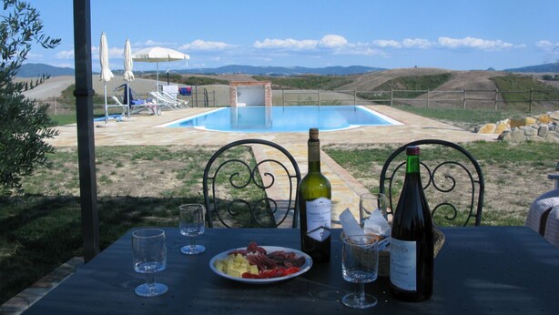 An outdoor dining area with a pool view, a bottle of wine, and a plate of food. - Belvilla by OYO Gatterino (Peccioli)