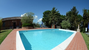 Una piscina rettangolare con bordi in mattoni, circondata da un prato e alberi.