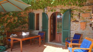 Un patio con una mesa y sillas de madera, una sombrilla verde y una pared de piedra cubierta de vegetación.