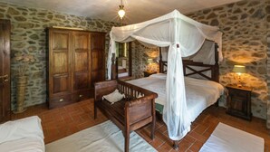 Un dormitorio con una cama con dosel, un banco de madera, una pared de piedra y un gran armario.