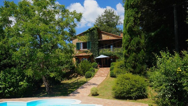 Un área de piscina con un camino de piedra que lleva a una casa rodeada de vegetación.
