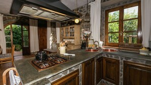 Una cocina con una isla de piedra, armarios de madera, una estufa a gas y un amplio ventanal con vistas al verdor.