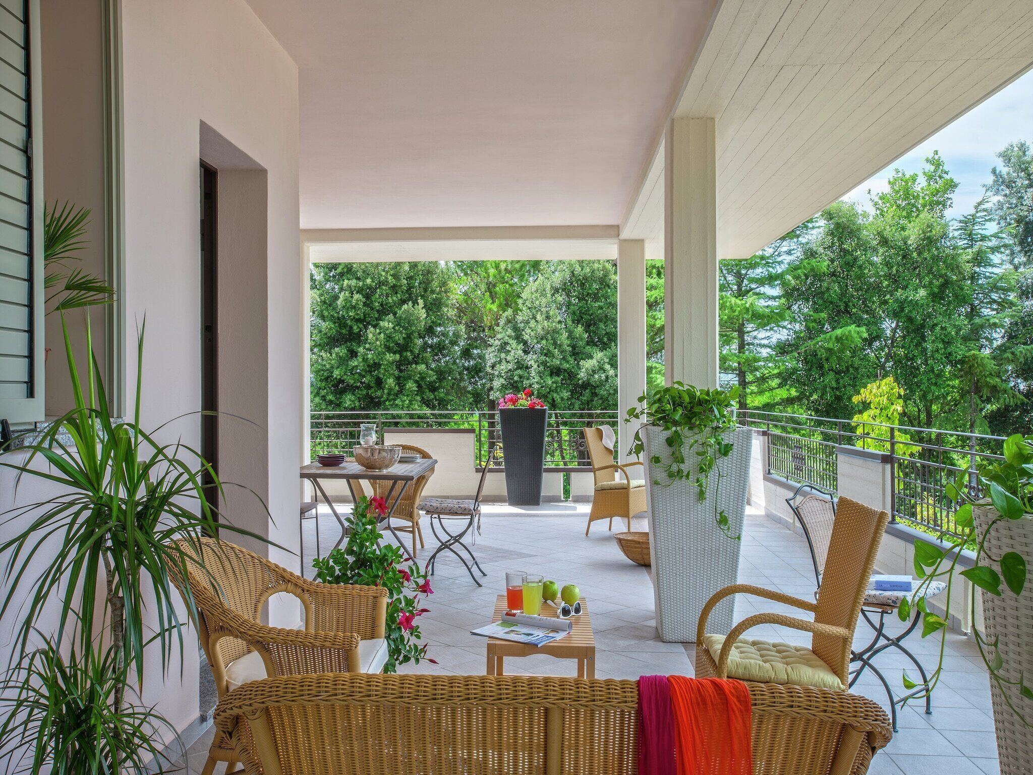 A covered outdoor area with wicker furniture, a table with drinks, and potted plants.