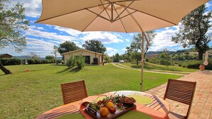 An outdoor patio with a table set for a meal, surrounded by chairs, and an umbrella providing shade. - Cottage in Montelabbate with Pool & Forest (Montelabbate)