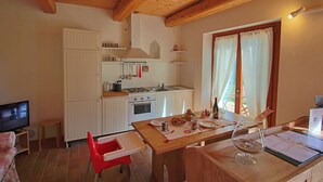 A compact kitchen with white cabinets, a wooden table set for dining, and a TV in the corner. - Cottage in Montelabbate with Pool & Forest (Montelabbate)