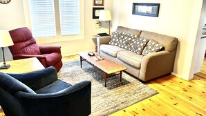 A living room with a red armchair, a blue armchair, a beige sofa with patterned cushions, a wooden coffee table, and a rug.