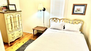 A bedroom with a bed, dresser, lamp, and framed pictures on the wall.