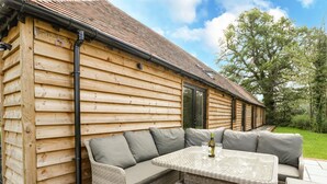 A log cabin with a patio area featuring wicker furniture and a table with a bottle and glasses. - The Old Dairy (Wokingham)