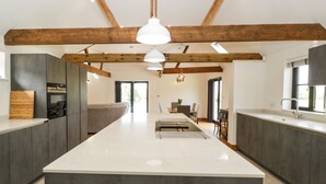 A modern kitchen with dark cabinetry, a large island, and exposed wooden beams. - The Old Dairy (Wokingham)
