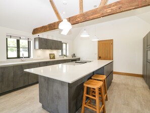 A modern kitchen with a large island, wooden stools, and exposed beams. - The Old Dairy (Wokingham)