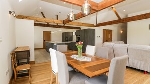 A modern interior with a wooden dining table, grey upholstered chairs, and a sofa. - The Old Dairy (Wokingham)