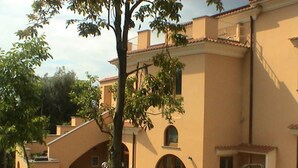 Un edificio con fachada color crema, varias ventanas y una escalera que lleva a un balcón.