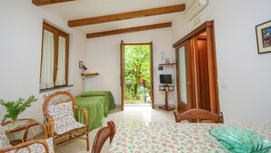 Una habitación con techo de madera, un sofá verde, una mesa de comedor con mantel floral, sillas de mimbre y un mueble de televisión con televisor.