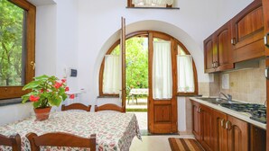A kitchen with wooden cabinets, a dining table with a floral tablecloth, and a potted plant.
