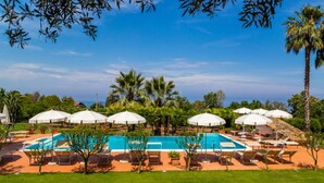 A pool area with white umbrellas, lounge chairs, and palm trees. - Belvilla by OYO Nicolֳ² (Ricadi)
