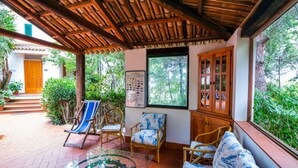 A covered patio with wicker furniture, a glass table, and a view of greenery. - Belvilla by OYO Nicolֳ² (Ricadi)