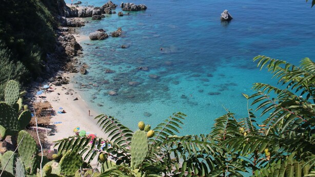 A coastal beach with clear turquoise water, rocky outcrops, and lush vegetation. - Belvilla by OYO Nicolֳ² (Ricadi)