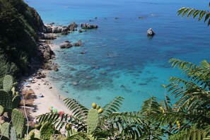 A coastal beach with clear turquoise water, rocky outcrops, and lush vegetation. - Belvilla by OYO Nicolֳ² (Ricadi)