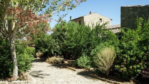 A stone building with a tiled roof, surrounded by dense greenery and a cobblestone path.