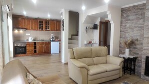 A modern living room with a beige sofa, a kitchen with wooden cabinets, and a stone wall. - Vacation home in Baixo Alentejo, with swimming pool and barbecue, half an hour from the Algarve (Santa Clara-a-Nova, Almodôvar)