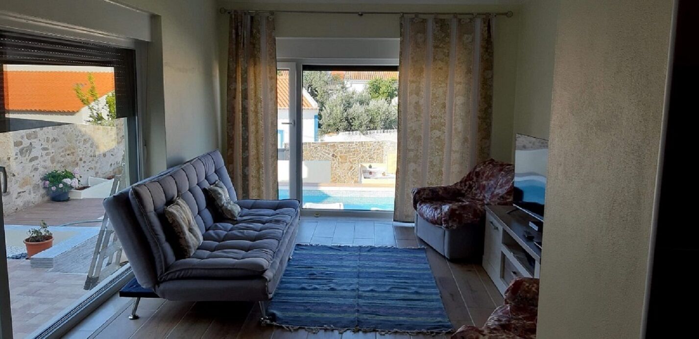 A living room with a sofa, a rug, and a television. There is a sliding glass door leading to an outdoor area with a pool.