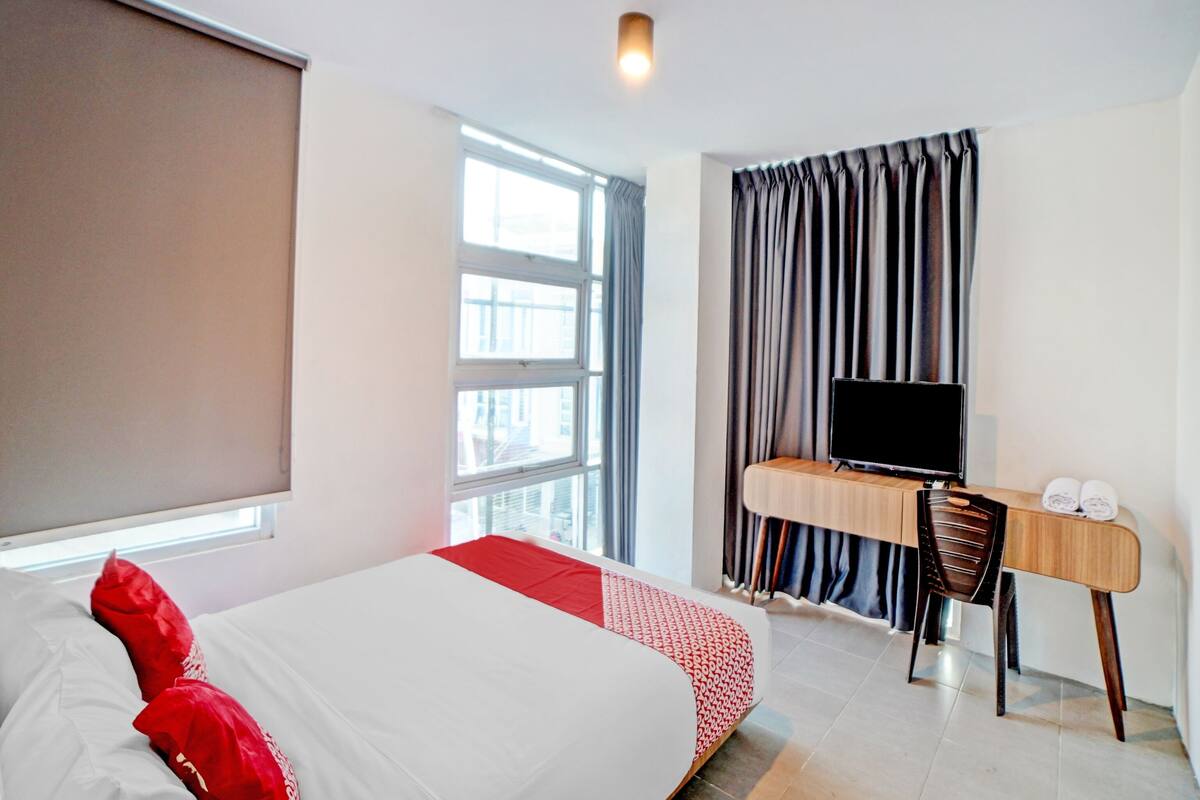 A hotel room with a bed, a desk with a TV, and a window with curtains.