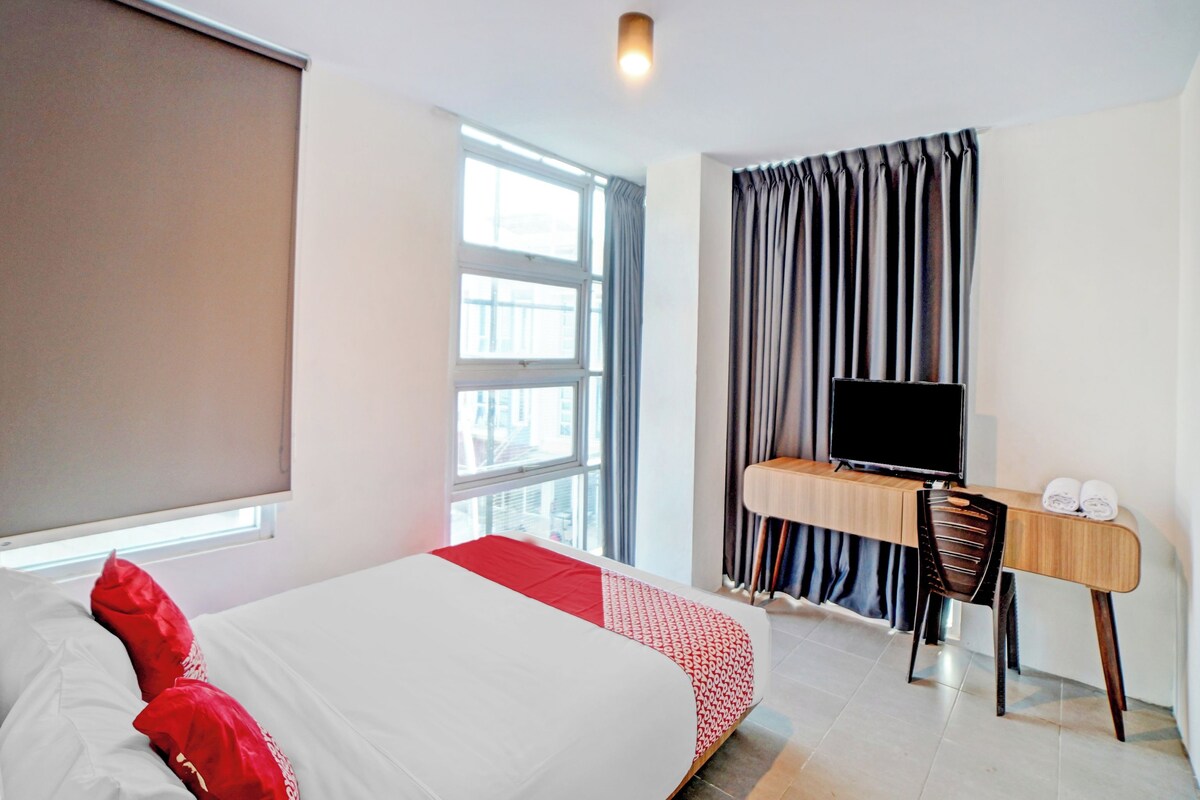 Una camera d'albergo con un letto, una scrivania con televisione e una finestra con tende.