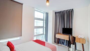 A hotel room with a bed, a desk with a TV, and a window with curtains.