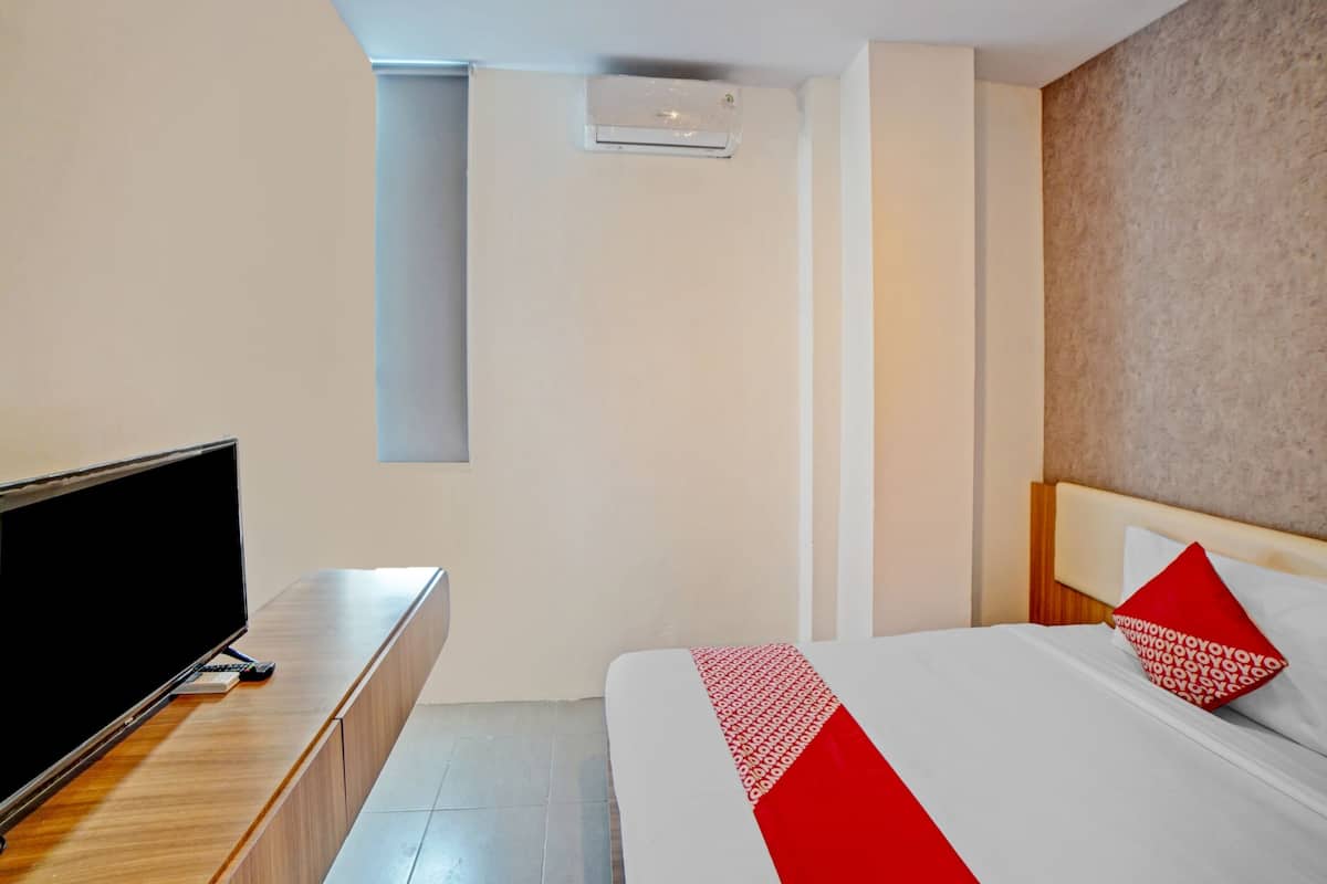 A hotel room with a bed, a TV on a wooden console, a red and white patterned bedspread, and a beige textured wall.