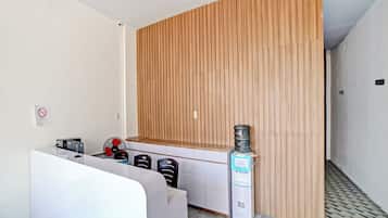 A modern hotel room with a wooden accent wall, a white reception desk, and a water dispenser.
