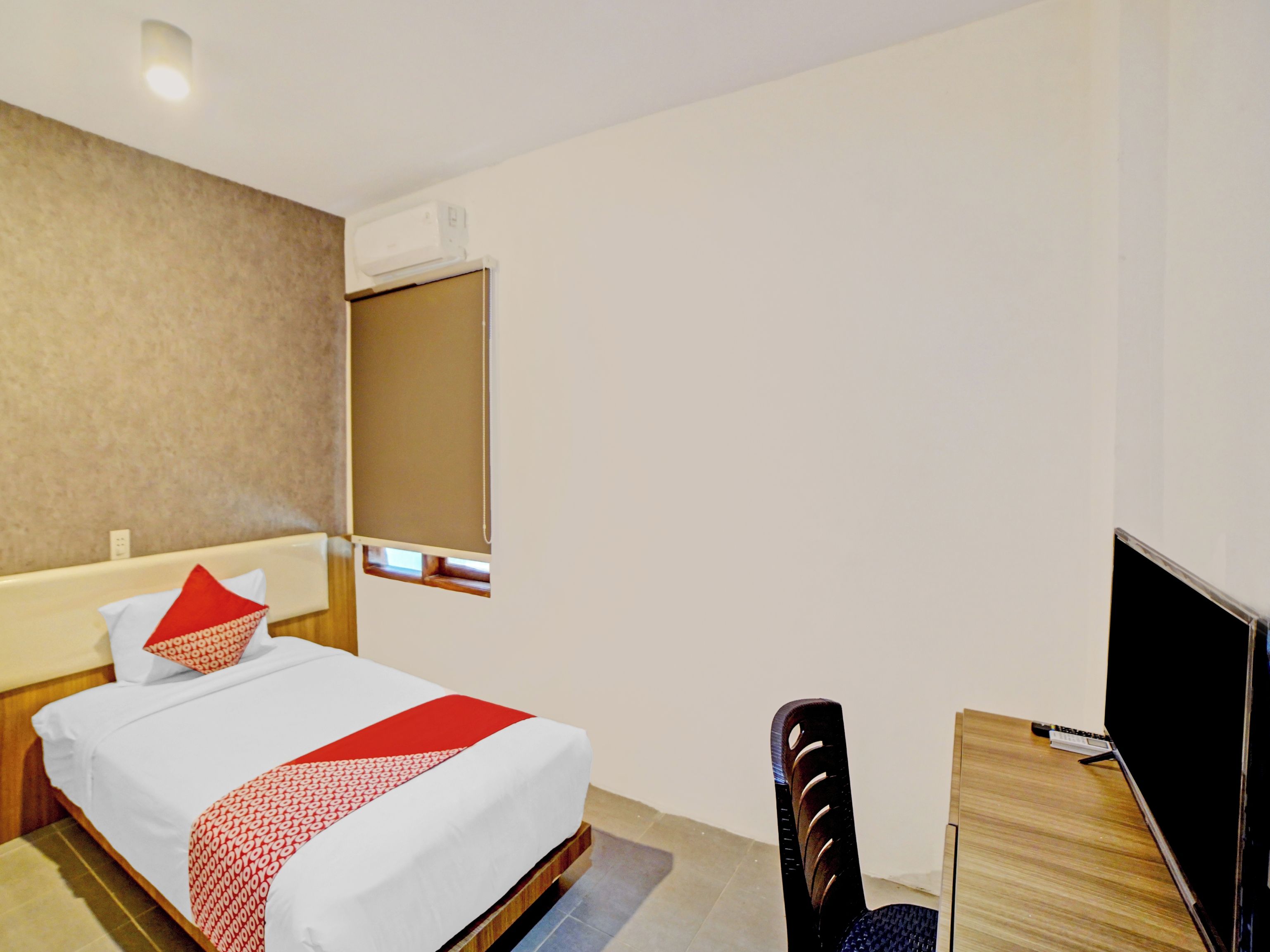 Habitación de hotel con cama, escritorio, silla, televisor y aire acondicionado.