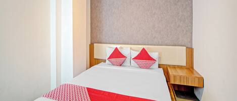 A hotel room with a bed, a wooden nightstand, and a headboard with a textured wall behind it.
