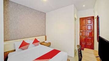 A hotel room with a bed, a wooden nightstand, a TV, and a door.